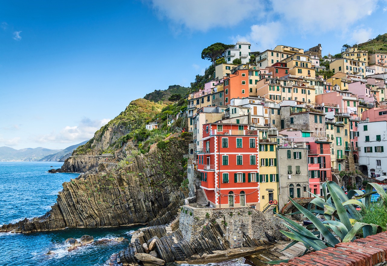 Vista panorámica de casas coloridas construidas en un acantilado junto al mar, rodeadas de naturaleza y cielo despejado.